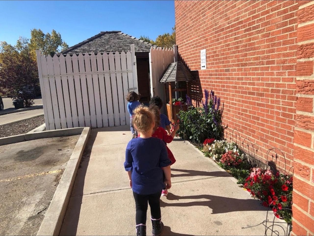 Children walking up the path to the Kids 'R' Us door beside the red-brick building and white fence